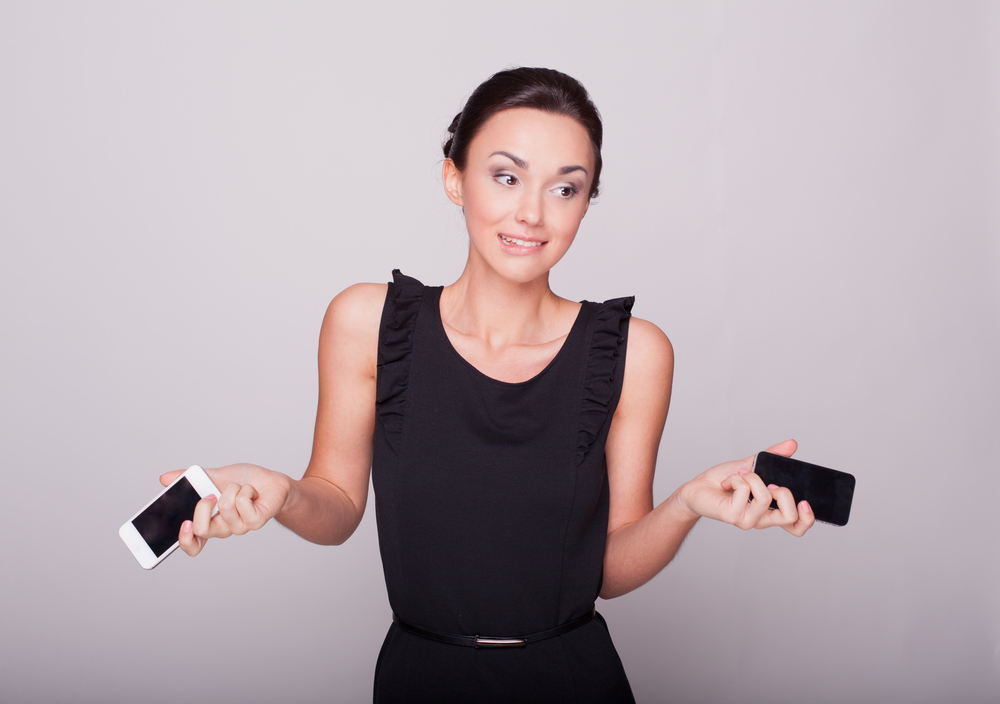 Woman holding two mobile phones - Shutterstock.